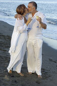 Middle-aged couple on the beach, holding champagne glasses