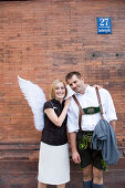 Angel, young woman with wings standing next to a man in traditional dress, Munich, Bavaria, Germany