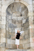 Mid adult woman wearing angel wings standing in alcove, Munich, Bavaria, Germany