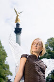 Mid adult woman wearing angel wings near Friedensengel, Munich, Bavaria, Germany