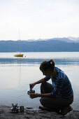 A young woman making a drink on a cooking stove at Lake Walchensee, Upper Bavaria, Bavaria, Germany