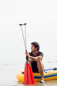 Young man sitting on a dinghy, lake Ammersee, Bavaria, Germany