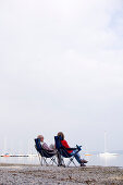 Older couple sitting on folding chairs on the beach at Lake Ammersee, Bavaria, Germany