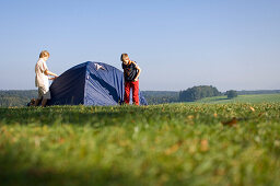 Two boys putting up a tent in a meadow, Camping, Bavaria, Germany