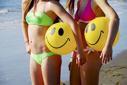 girl 13, girl 18 yrs standing on beach holding smile beach balls