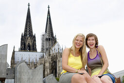 Two young women smiling at camera, Cologne Cathedral in background, Cologne, North Rhine-Westphalia, Germany