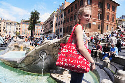 Young woman with a red Roma bag at Fontana della Barcaccia on Piazza di Spagna, Spanish Steps in background, Rome, Italy