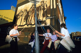 Children playing in front of a painted wall of a house, Falls Road, Belfast, County Antrim, Ireland, Europe