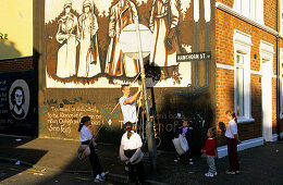 Children playing in front of a painted wall of a house, Falls Road, Belfast, County Antrim, Ireland, Europe