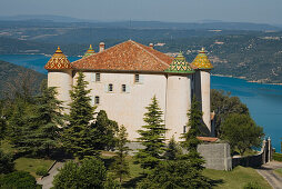 The castle of Aiguines with its coloured roof tiles in front of the lake Lac de Ste. Croix, Var, Provence, France