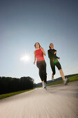 Two women running along road, Strasslach-Dingharting, Bavaria, Germany