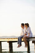 Paar sitzt auf einem Steg, Ambach, Starnberger See, Bayern, Deutschland