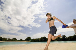 Teenage boy with bucket of water running after girlfriend, Freising, Bavaria, Germany