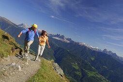 Couple holding hands running over hiking trail, Dolomites in background, South Tyrol, Italy