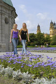 Two young women in Hofgarten, Theatine Church in background, Munich, Bavaria, Germany
