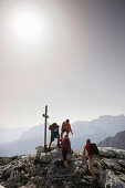 Hikers arriving summit cross, Wetterstein range, Bavaria, Germany