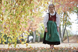 A girl wearing a Dirndl dress standing below a tree, Kaufbeuren, Bavaria, Germany