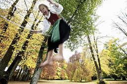 Mädchen im Dirndl schaukelt im Park, Kaufbeuren, Bayern, Deutschland