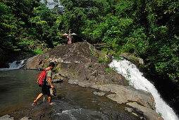Ein Mann watet durch einen Fluss nahe eines Wasserfalls, Nord Bali, Indonesien, Asien