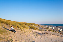 Frau sitzt in einer Düne, Rantum, Sylt, Nordfriesland, Schleswig-Holstein, Deutschland
