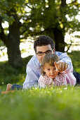 Father and daughter (2-3 years) lying in meadow, English Garden, Munich, Bavaria, Germany