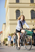 Businesswoman riding bicycle at Odeonsplatz, Munich, Bavaria, Germany
