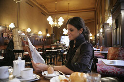 Frau mittleren Alters beim Frühstück in einem Café liest Zeitung, Wien, Österreich