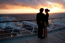 Junges Paar schaut sich den Sonnenuntergang an, Passagiere auf dem Achterdeck, Kreuzfahrtschiff Queen Mary 2, Transatlantik, Nordatlantik, Atlantik