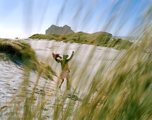 Woman running over a dune in the sunlight, Wharariki Beach, North coast, South Island, New Zealand