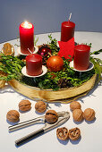 Adventskranz mit einer brennenden Kerze, mit Nussknacker und Walnüssen im Vordergrund