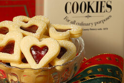 Christmas cookies raspberry hearts covered with sugar piling up in glasbowl, Christmas decoration in background