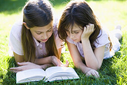 Two girls reading a book laying on the grass