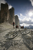 Three persons resting, mountain bikes in foreground, Tre Cime di Lavaredo, Veneto, Italy