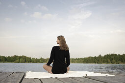 Junge Frau sitzt auf einem Steg am Starnberger See, Bayern, Deutschland