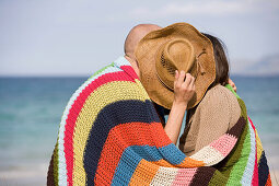 Adult, Adults, beach, beaches, Blanket, Blankets, Color, Colour, complicity, Contemporary, couple, couples, Cover, Covering, Daytime, exterior, female, Hat, Hats, Headgear, Hold, Holding, human, Intimacy, kiss, kisses, kissing, Leisure, love, male, man, m