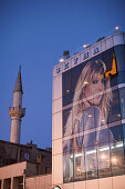 Geschäftshaus mit Dachterrasse in Üsküdar, Bosporos mit riesigem beleuchteten Werbeposter einer blonden Frau, Mode, im Hintergrund das Minarett der Moschee, Istanbul