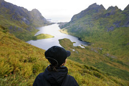 Junge Frau schaut auf den von Bergen umgebenen See Agvatnet, Lofoten, Norwegen, Skandinavien, Europa