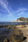 Paar am Strand Blick auf Cefalu mit Rocca di Cefalu, Cefalu, Sizilien, Italien