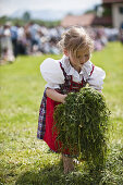 Mädchen (4-6 Jahre) im Dirndl mit Gras in den Händen, Mailaufen, Antdorf, Oberbayern, Deutschland