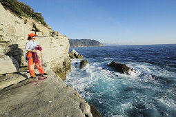Frau hält Seil in der Hand und bereitet sich auf Klettern vor, Steilküste am Mittelmeer, Ligurien, Italien