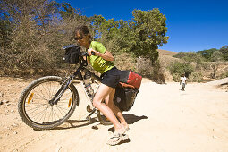 Frau schiebt Mountainbike bergauf auf einer Sandpiste, Madagaskar