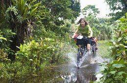 Woman cycling through shallow waters, Masoala National Park, Madagascar