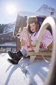 Kleinkind auf einem Schlitten vor einer Hütte, Galtür, Paznauntal, Tirol, Österreich