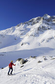 Female backcountry skier ascending to Hocharn, Hoher Sonnblick in background, Rauris valley, Goldberg mountain range, Hohe Tauern, Salzburg state, Austria