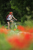 Radfahrerin, Mohnblumen im Vordergrund, Altmühltal-Radweg, Naturpark Altmühltal, Altmühltal, Bayern, Deutschland