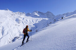 Woman backcountry skiing, ascending mountain towards Hohe Warte, Olperer in background, Hohe Warte, Schmirntal valley, Tuxer Alpen range, Tyrol, Austria