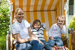 Mother with two children sitting in a roofed wicker beach chair, Hamburg, Germany