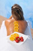Schale mit Orangen und Erdbeeren auf dem Rücken einer jungen Frau für eine natürliche Schönheitsbehandlung