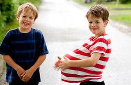 Zwei Jungen (6 -7 Jahre), einer versteckt einen Ball unter dem T-Shirt