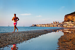 Jogger at beach,  old town, cathedral and cliff La Rocca, Cefalú, Palermo, Sicily, Italy